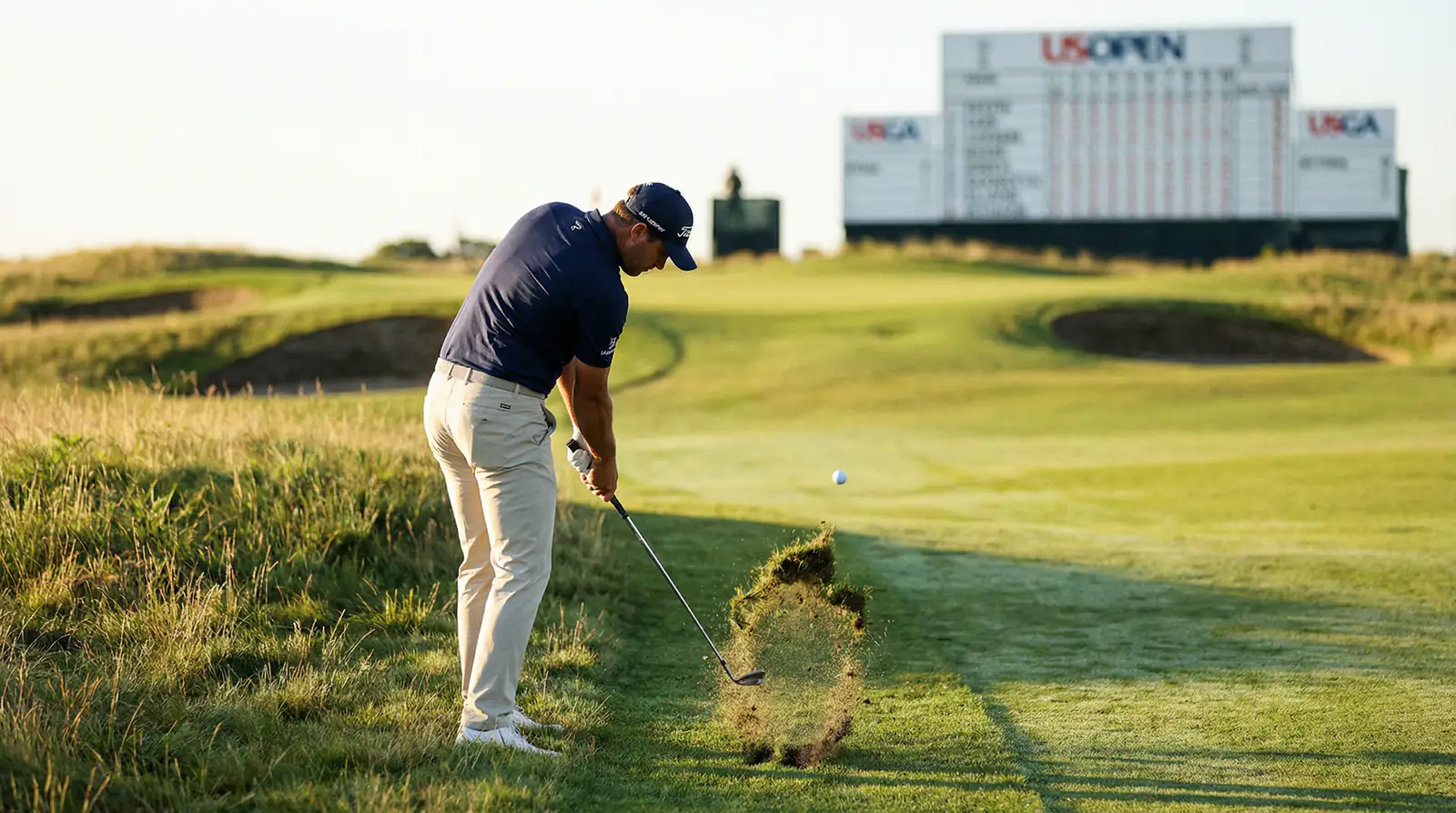 Golfista ejecutando un golpe desde el rough alto en un campo preparado para el US Open